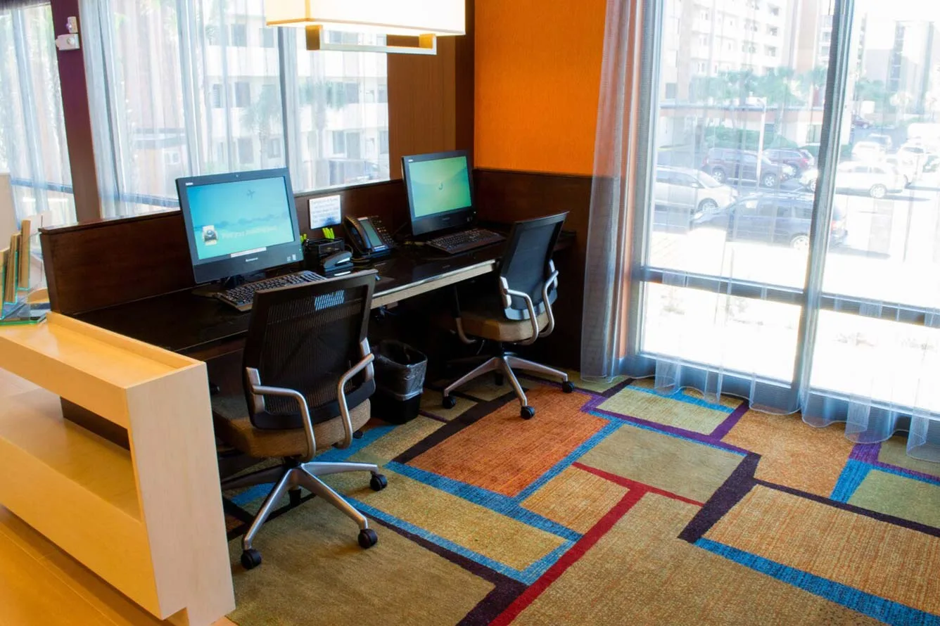 Espacio representativo del hotel: Una zona de trabajo compartida tiene puestos con computadoras junto a grandes ventanas.