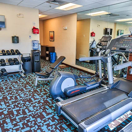 Espacio representativo del hotel: Un gimnasio con cintas de correr, bicicletas estáticas y una estantería de pesas.