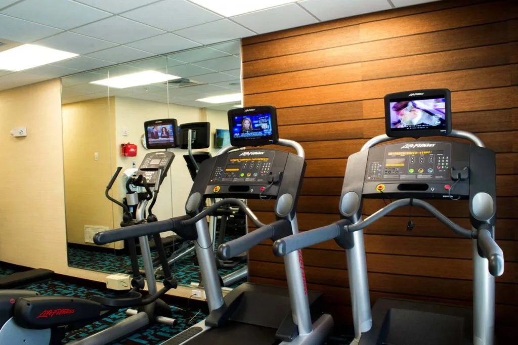 Espacio representativo del hotel: Un gimnasio con cintas de correr y otros equipos de ejercicio frente a una pared con espejos.