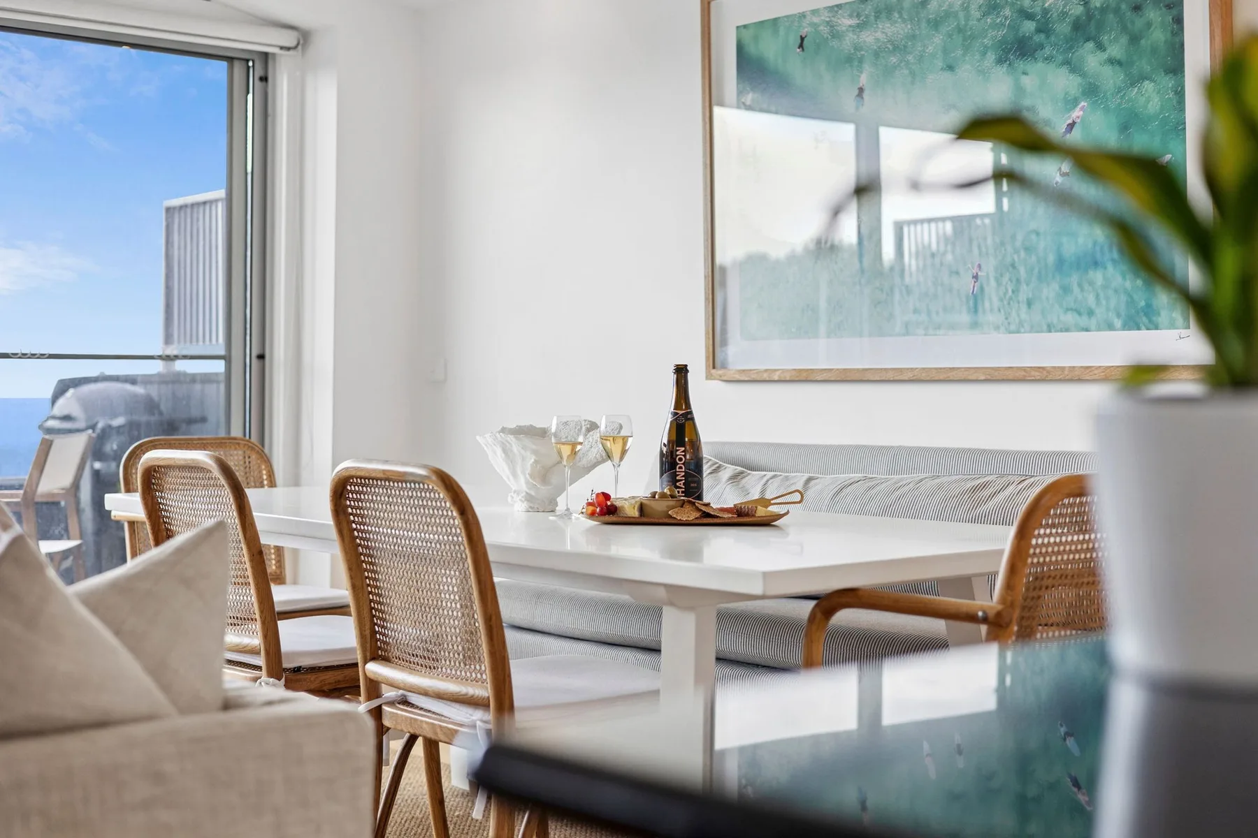 A bright dining area with a white table, woven chairs, and a large framed artwork.