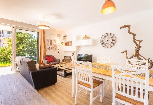 A bright living and dining area with a sofa, dining table, and glass doors to a garden.