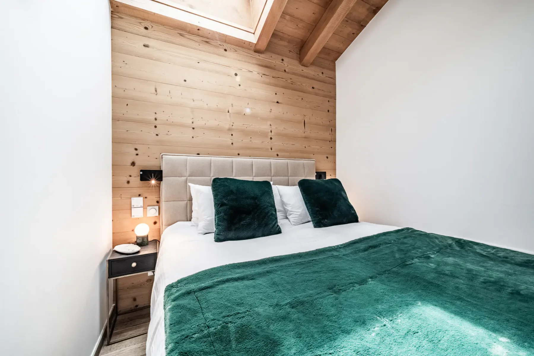 Un dormitorio con una cama vestida con ropa blanca y una manta verde oscuro.