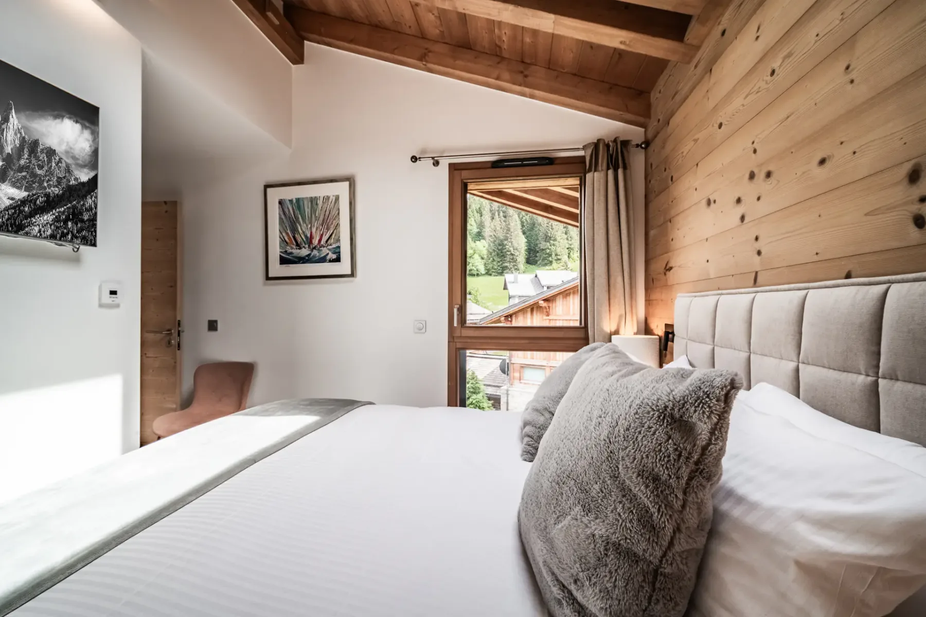 Un dormitorio con una cama grande, una pared revestida de madera y una ventana con vistas a la vegetación.