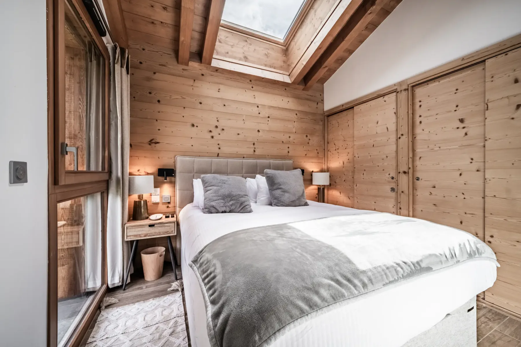 Un dormitorio con una cama bajo un gran tragaluz y vigas de madera a la vista.