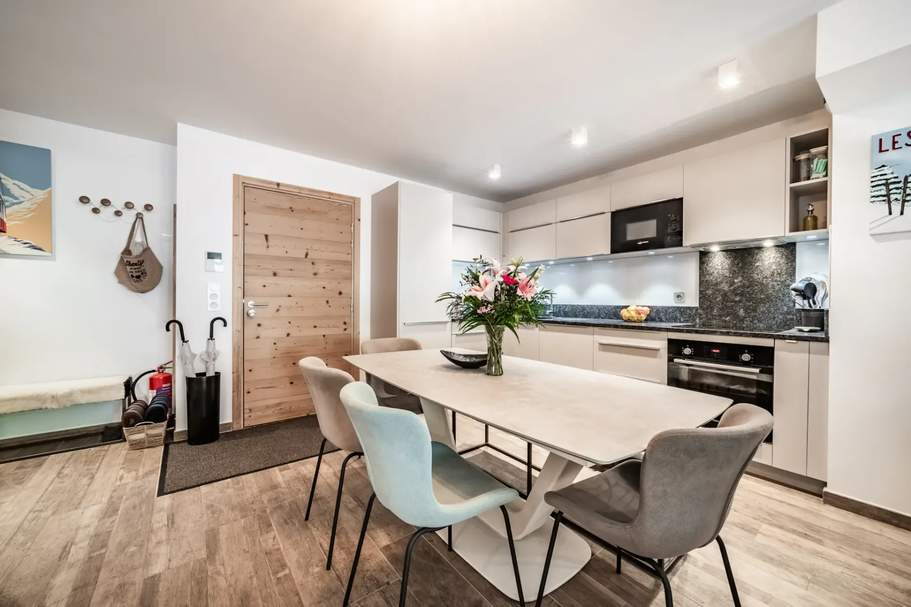 Un comedor se comunica con una cocina moderna, con una mesa y un arreglo floral.