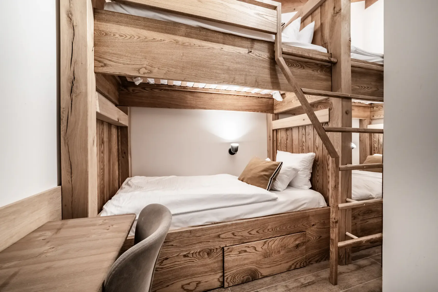 Una litera de madera ocupa el dormitorio, con ropa de cama blanca y una escalera.
