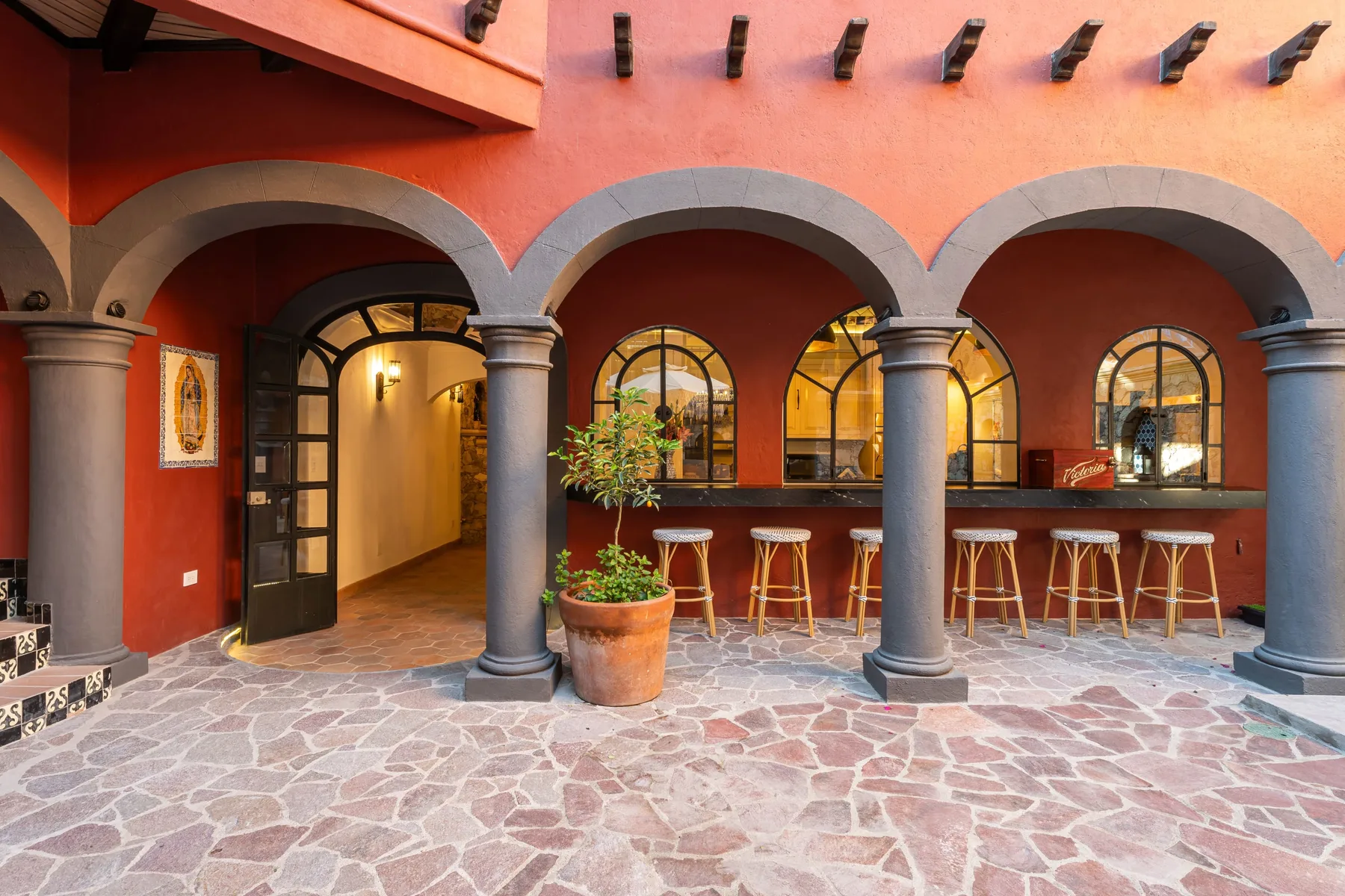 A red-walled courtyard features stone arches and a bar counter with stools.