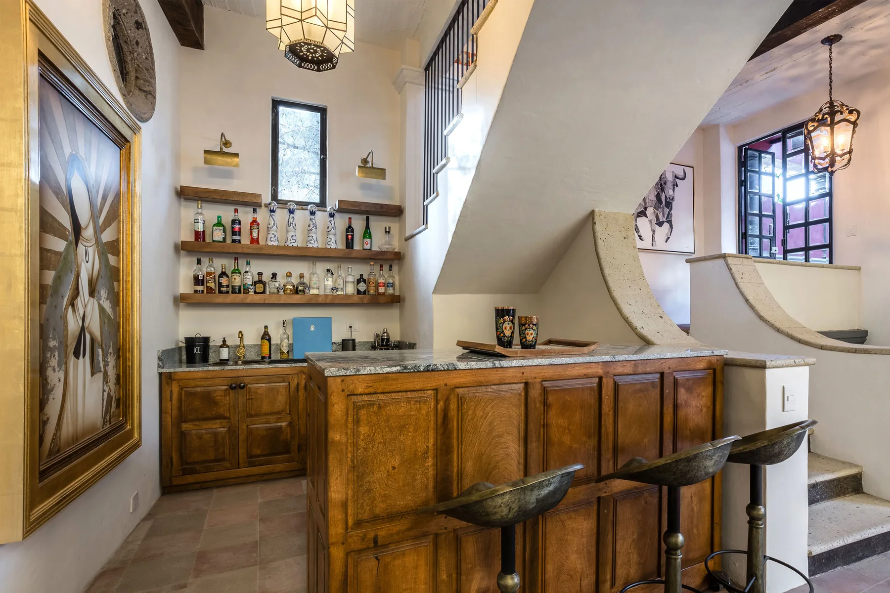 A home bar with wooden cabinetry and shelves of bottles beneath a staircase.