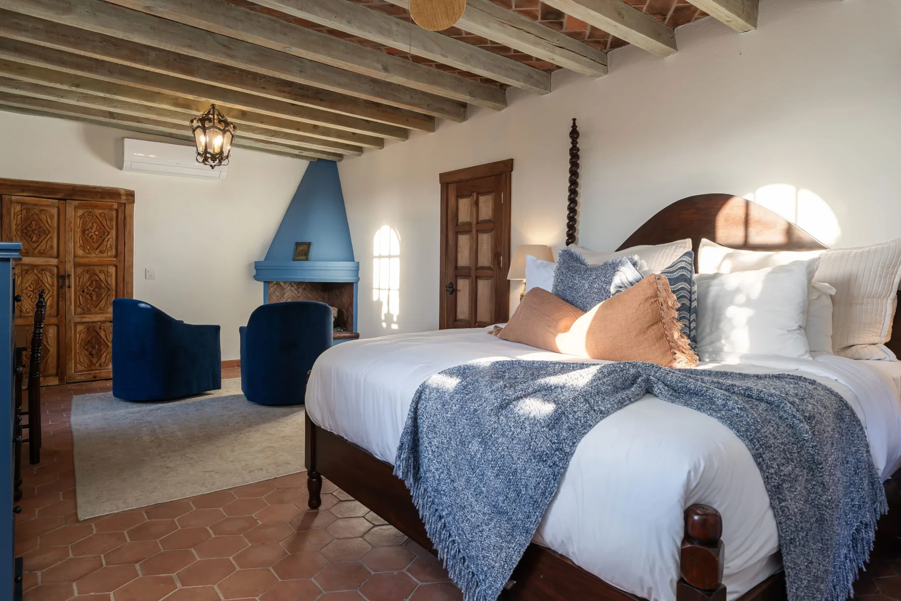 A bedroom with a bed, blue chairs, and exposed ceiling beams.