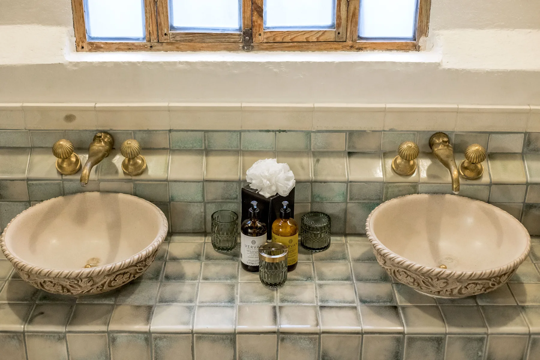 A tiled bathroom vanity with two sinks beneath a window.