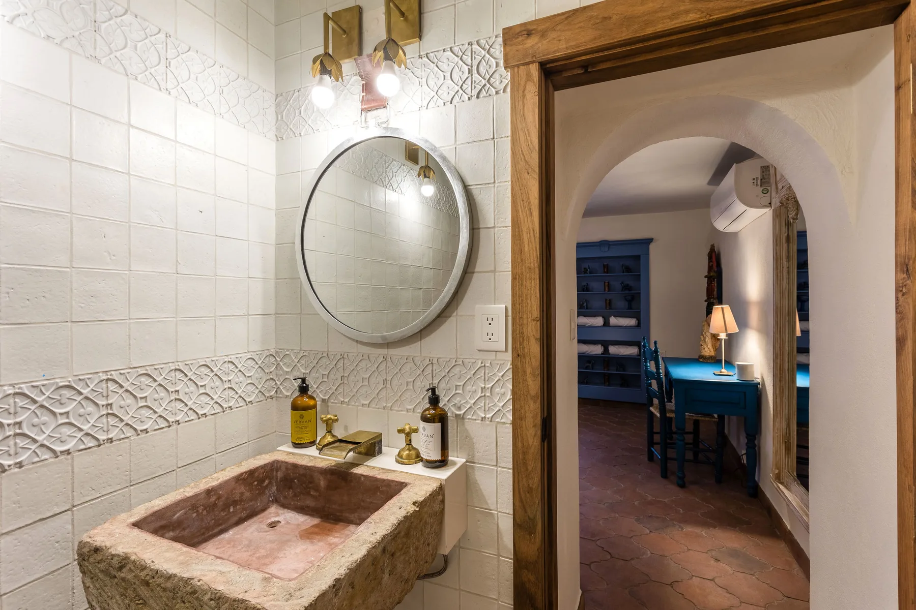 A tiled bathroom vanity with a stone basin opens onto a room with a desk.