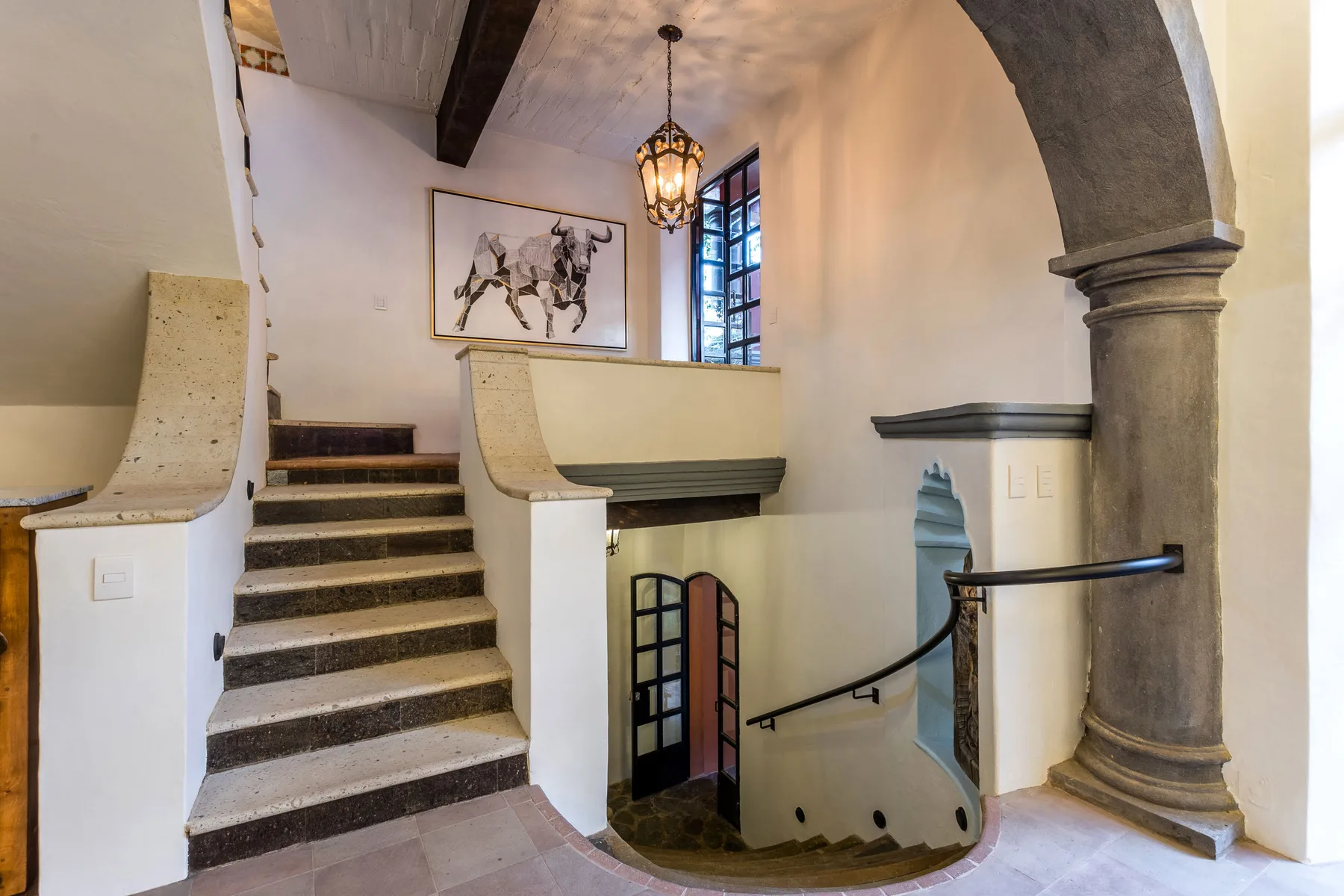 An interior staircase descends beneath a stone arch, with a hanging lantern overhead.