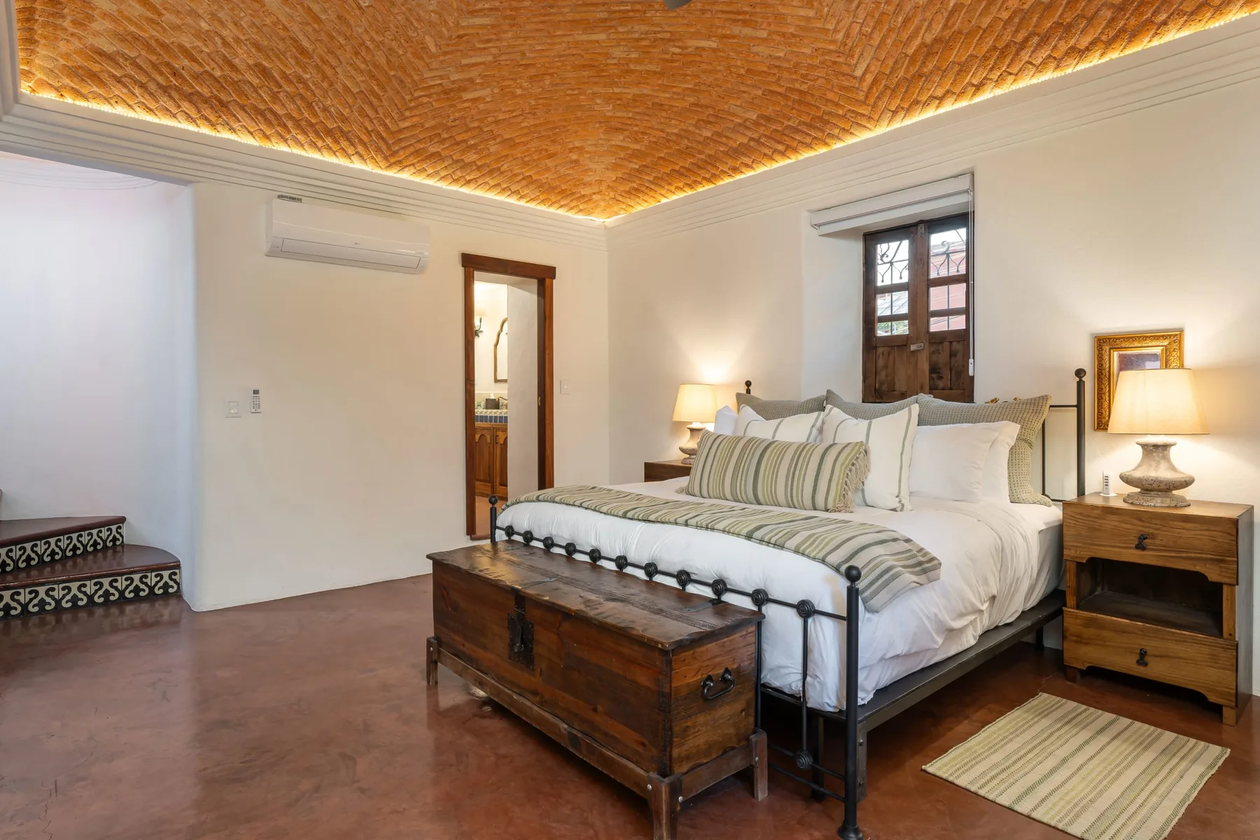 A bedroom with a large bed, wooden chest, and woven ceiling.
