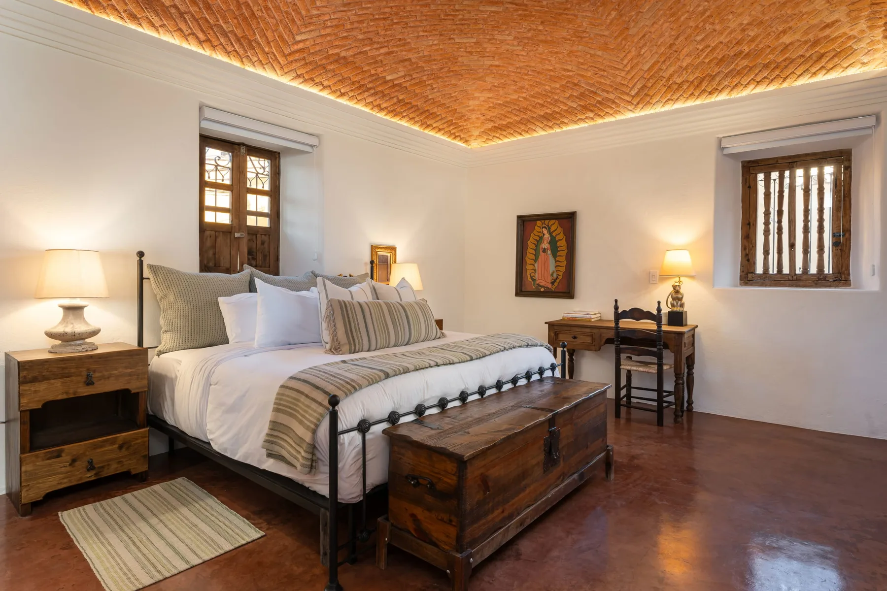 A bedroom with a large bed, wooden chest, and warm patterned ceiling.