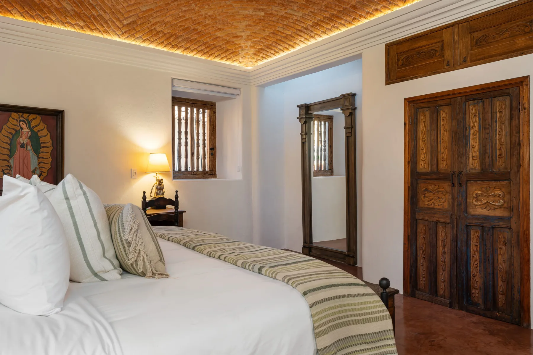 A bedroom with a white bed, wooden door, and standing mirror.