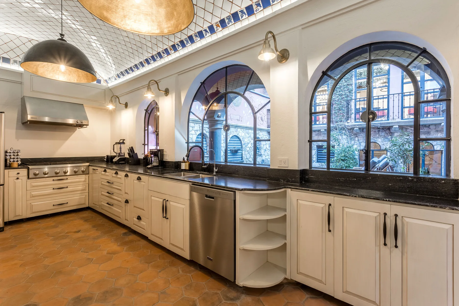 A bright kitchen with light cabinetry, dark countertops, and arched windows.
