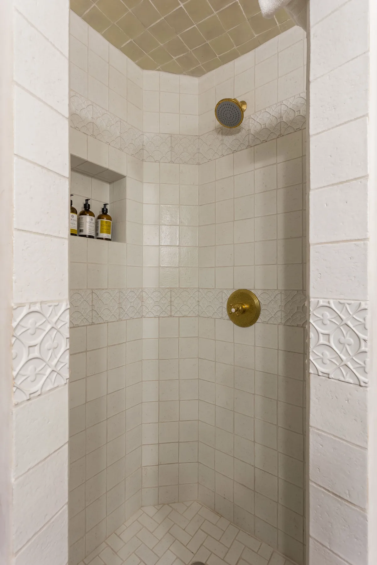 A tiled shower with a recessed shelf holding toiletries.