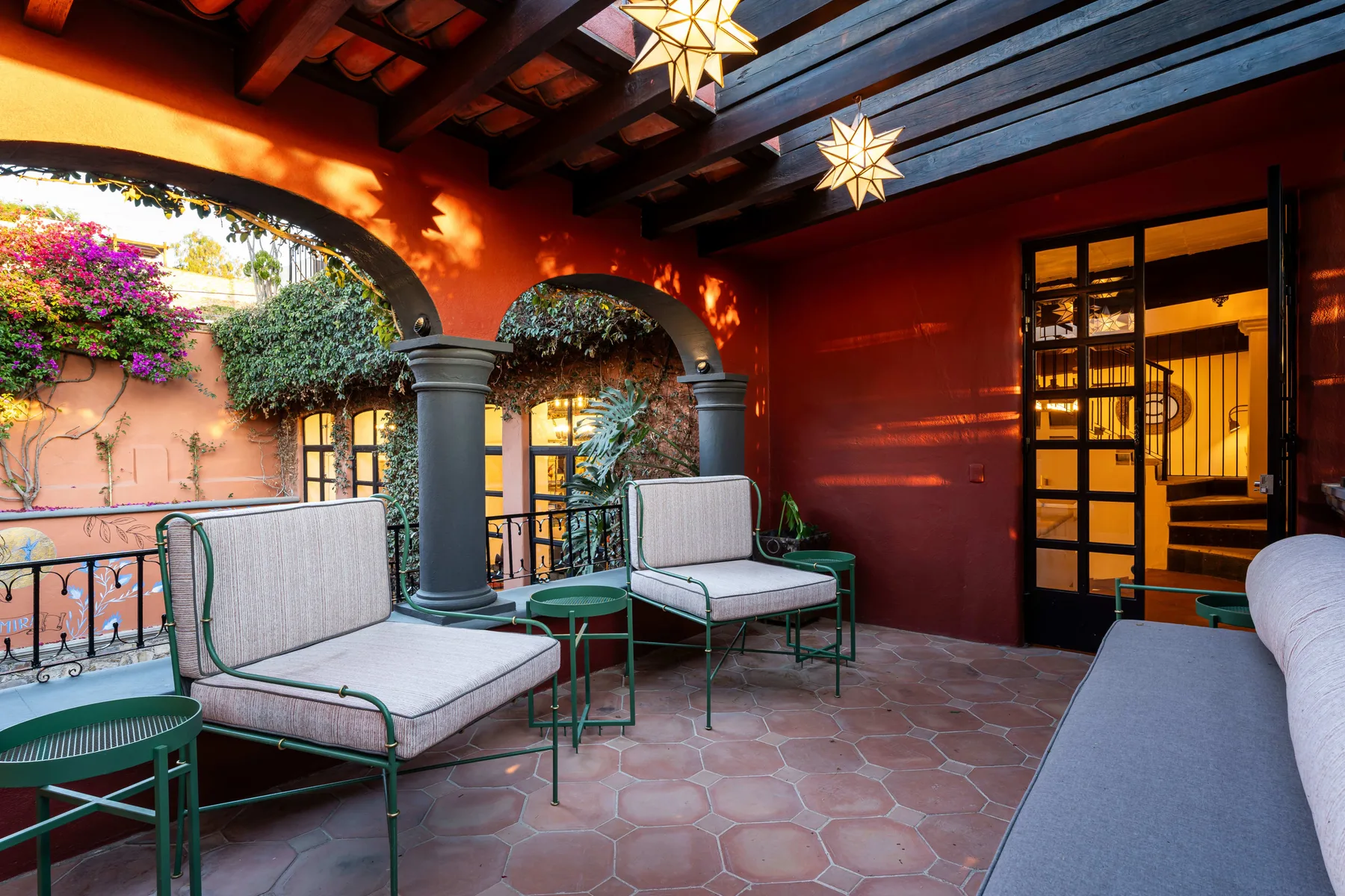 A covered patio with seating, tiled flooring, and arched openings.