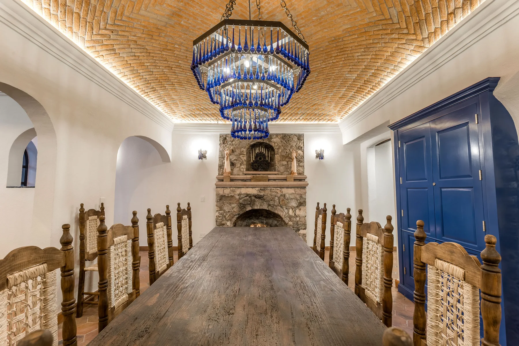 A dining room with a long wooden table, carved seating, and a stone fireplace.