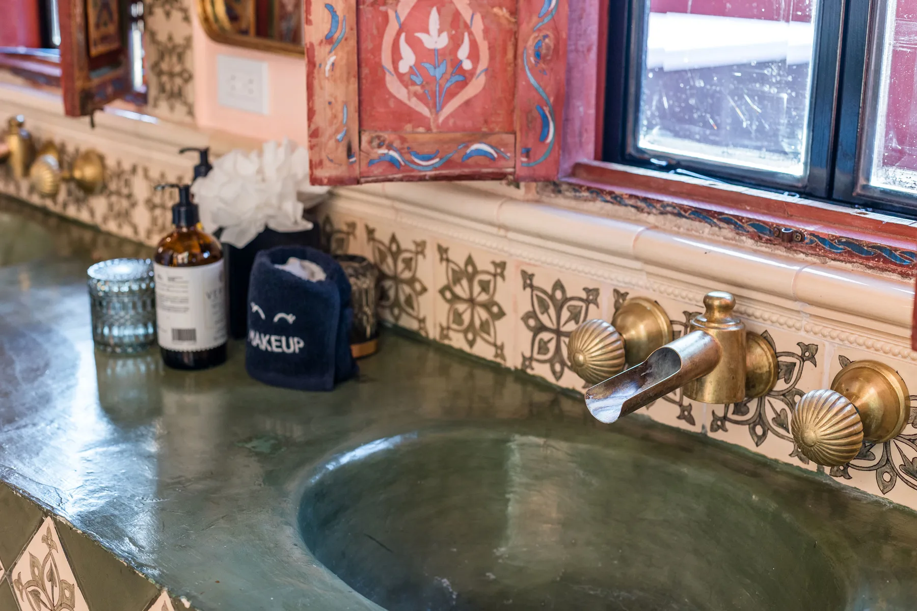 A bathroom vanity with a green countertop, basin, and decorative backsplash.
