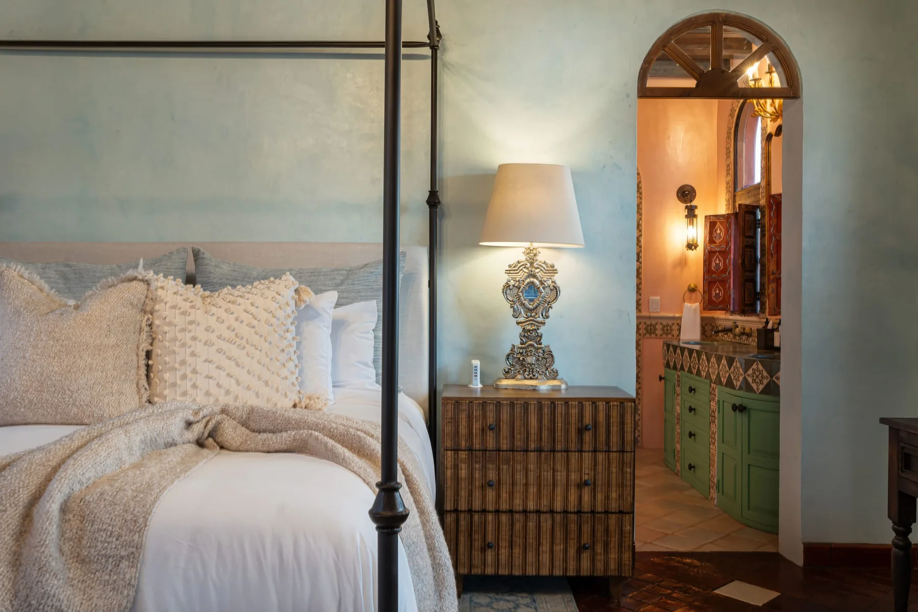 A bedroom with a four-poster bed beside an arched doorway.