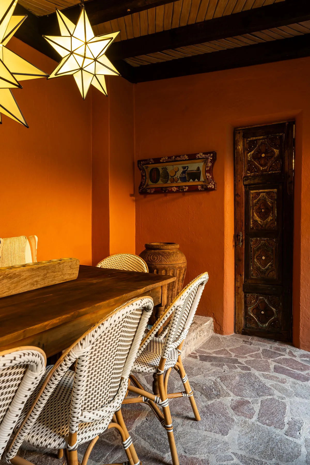 A dining area with a long wooden table and woven seating beneath star-shaped lights.