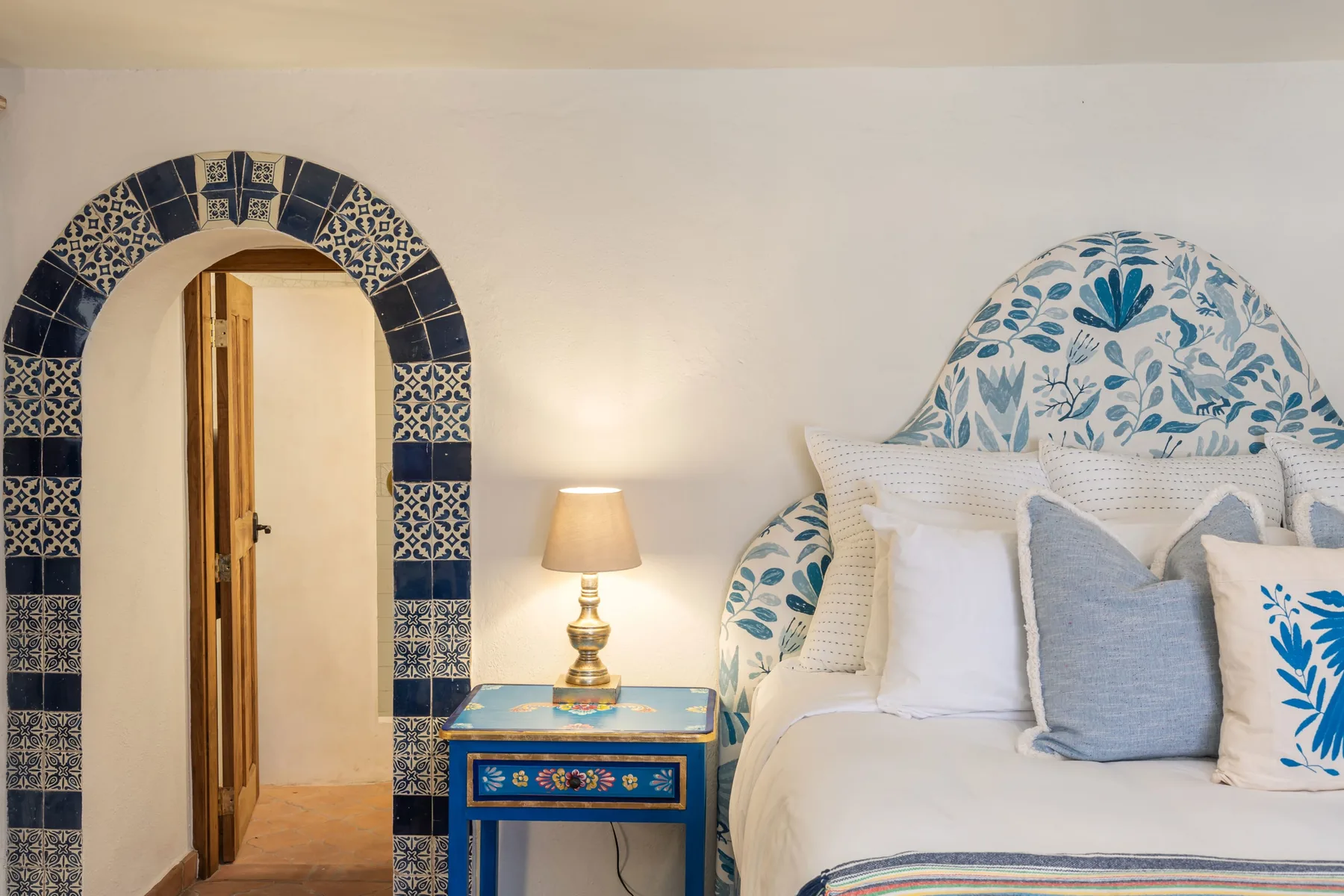 A bedroom with a bed, patterned headboard, and blue bedside table.