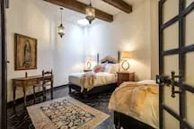 A bedroom with two beds, bedside tables, and patterned rugs.