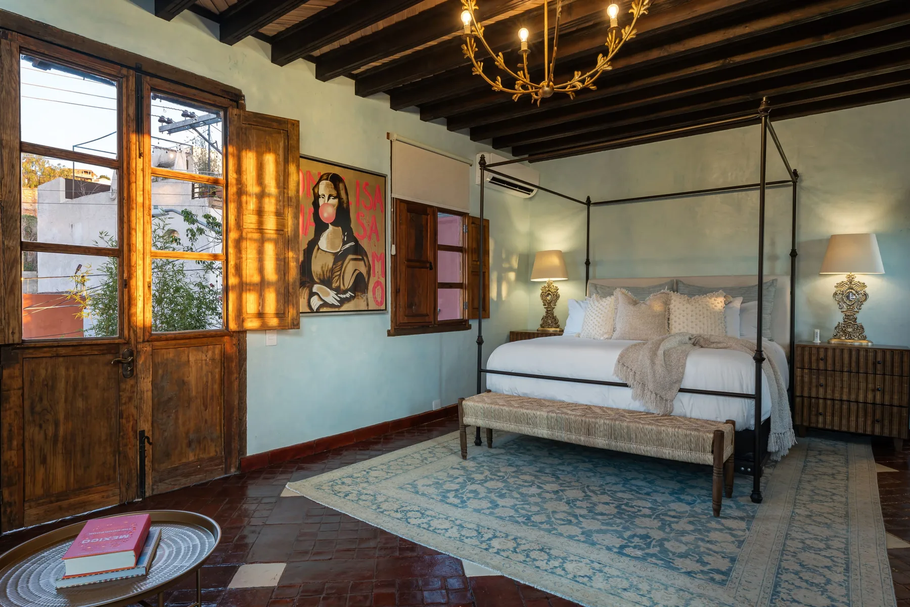 A bedroom with a white bed beneath dark exposed ceiling beams.
