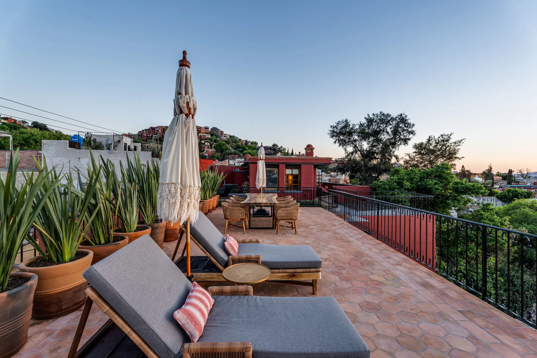 A rooftop terrace with cushioned seating, potted plants, and a closed umbrella.