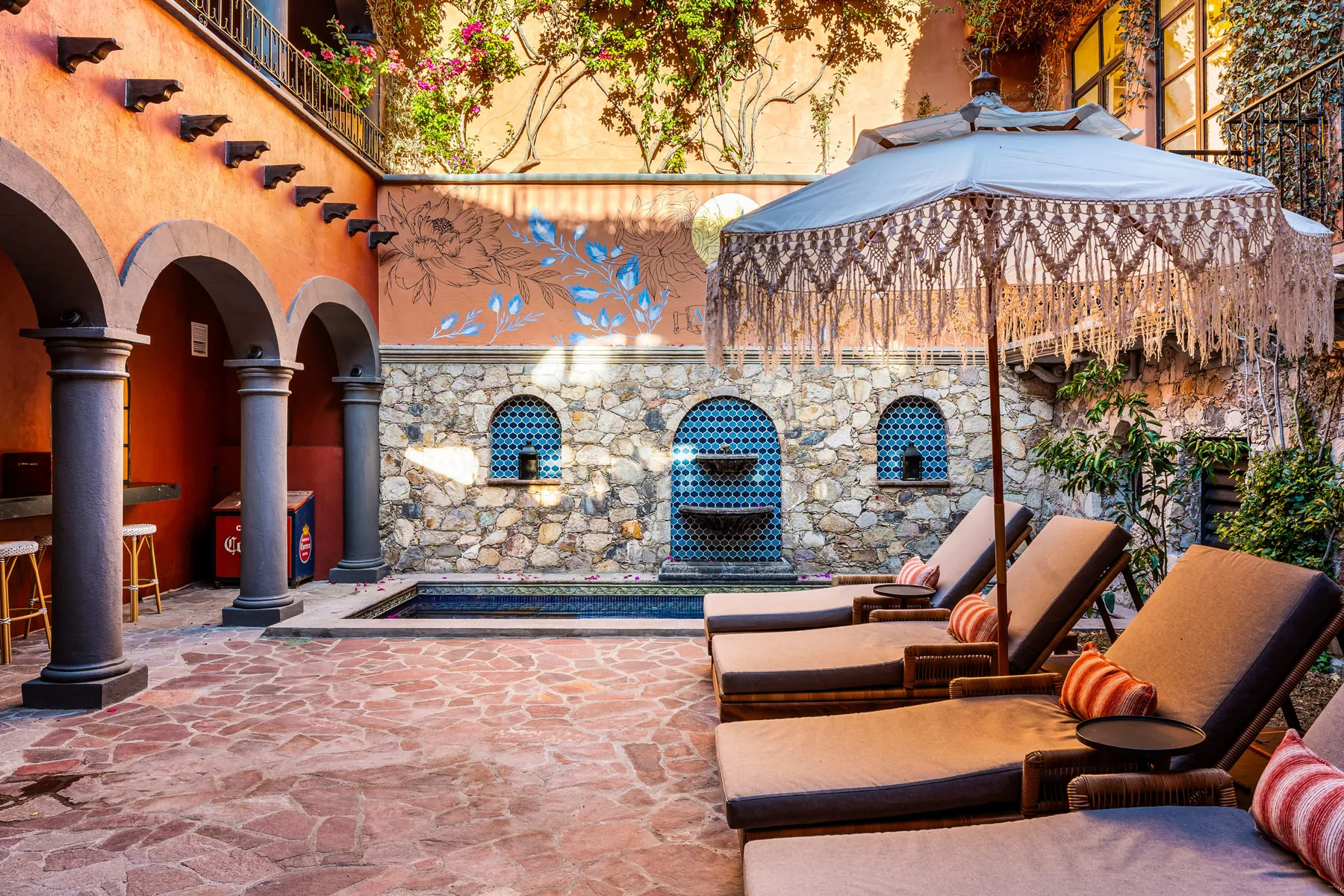 A courtyard pool area with lounge seating and a large fringed canopy.