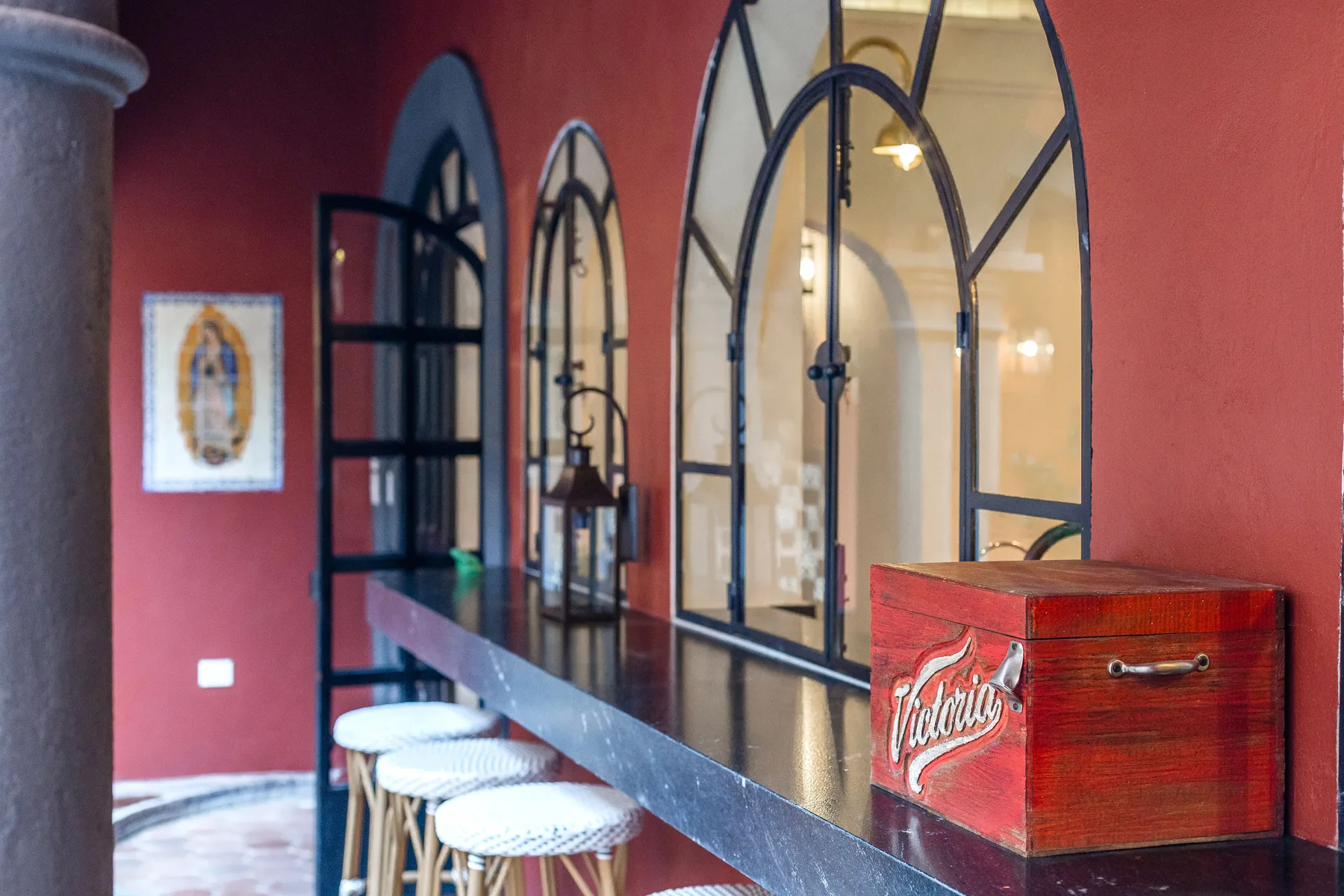 A bar counter sits beside tall arched windows in a red-walled interior.