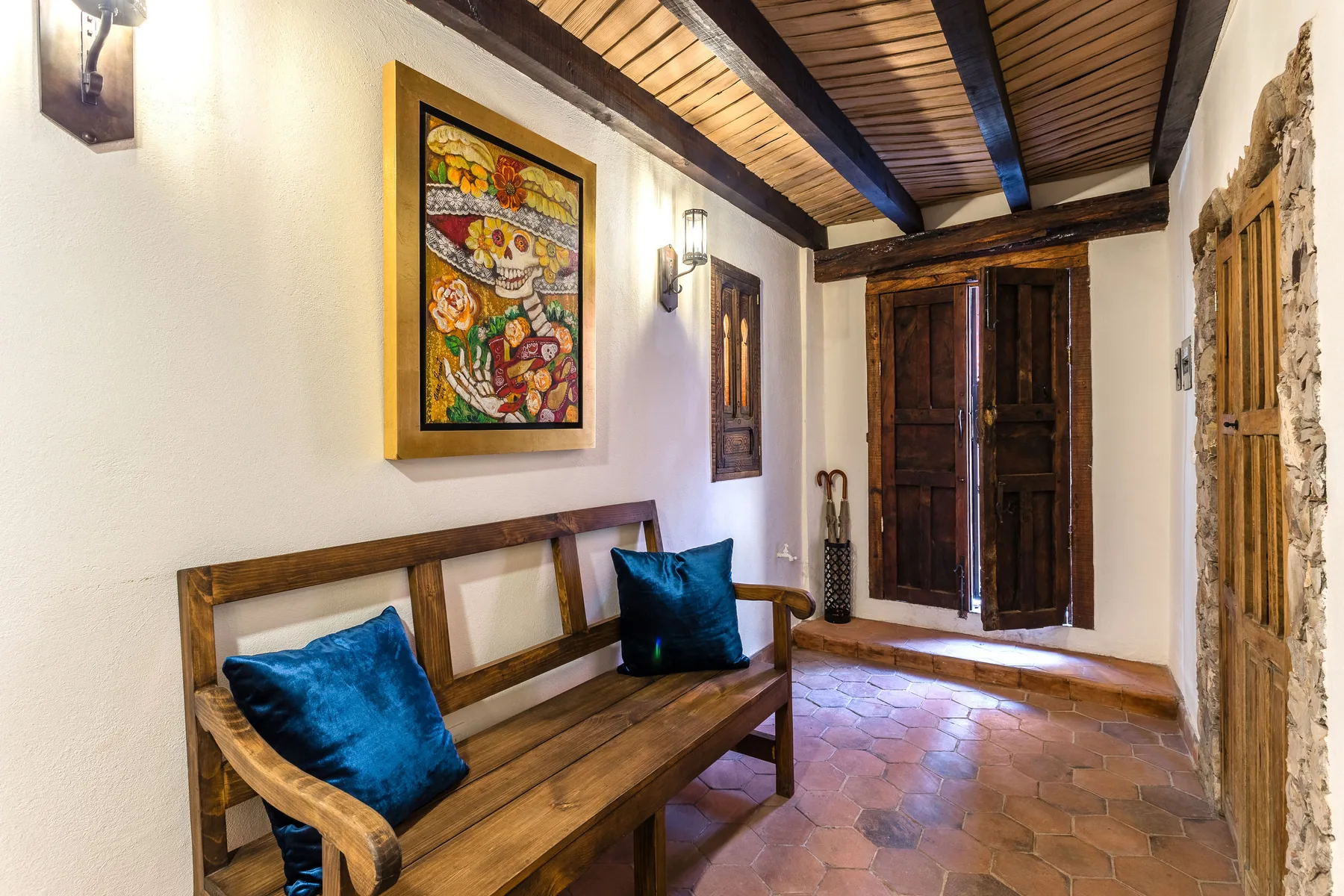 A rustic hallway with a wooden bench and colorful framed artwork.