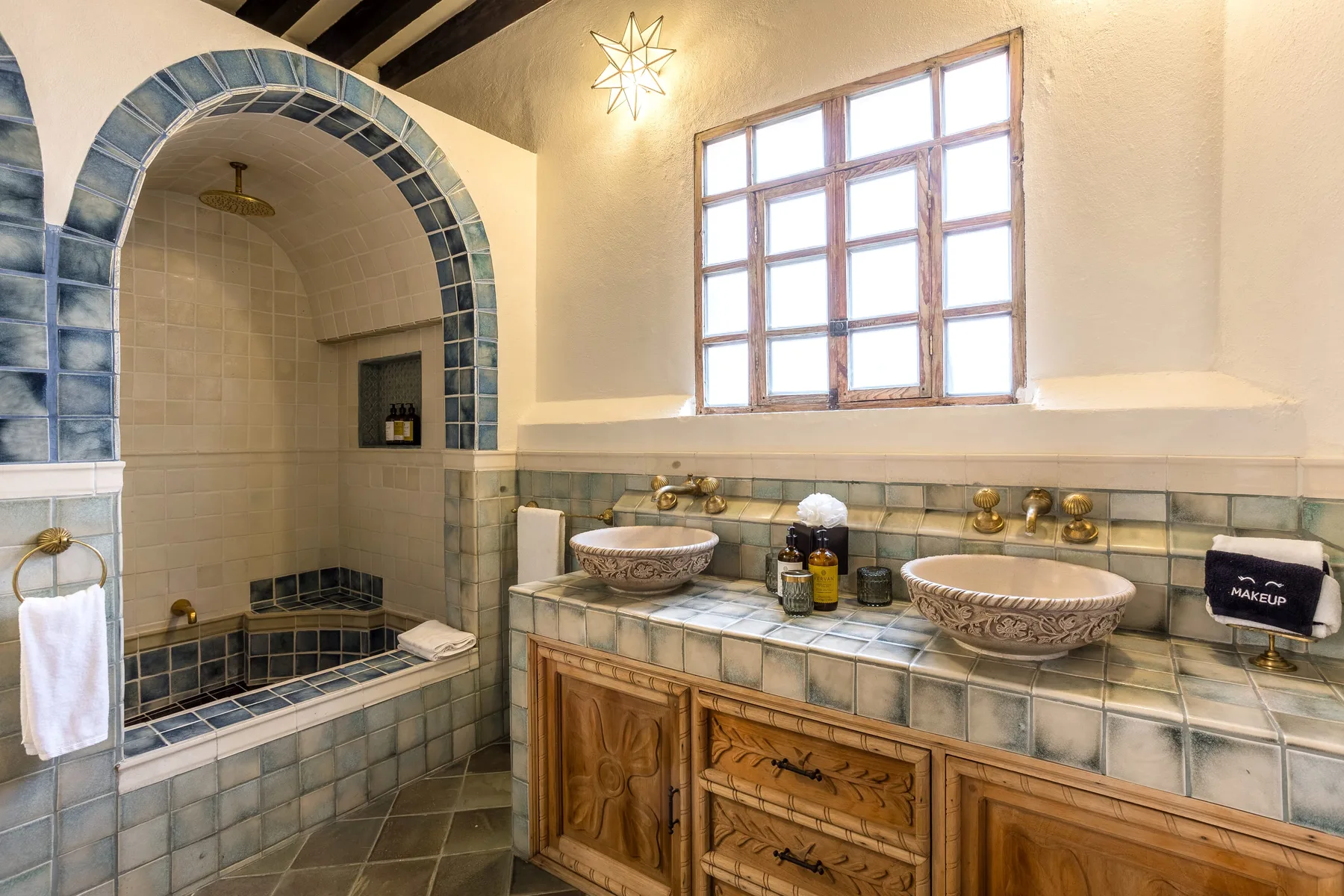 A tiled bathroom with an arched shower area and a double-sink vanity.