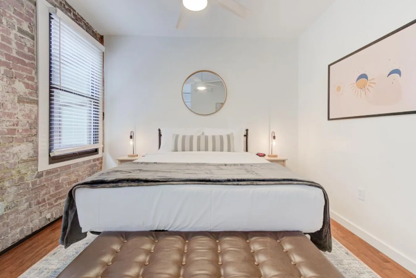 A bedroom with a neatly made bed beneath a round wall mirror.