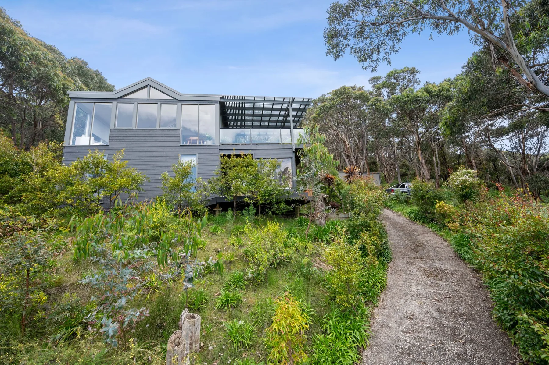 Una casa moderna se encuentra junto a un sendero rodeado de árboles y vegetación.