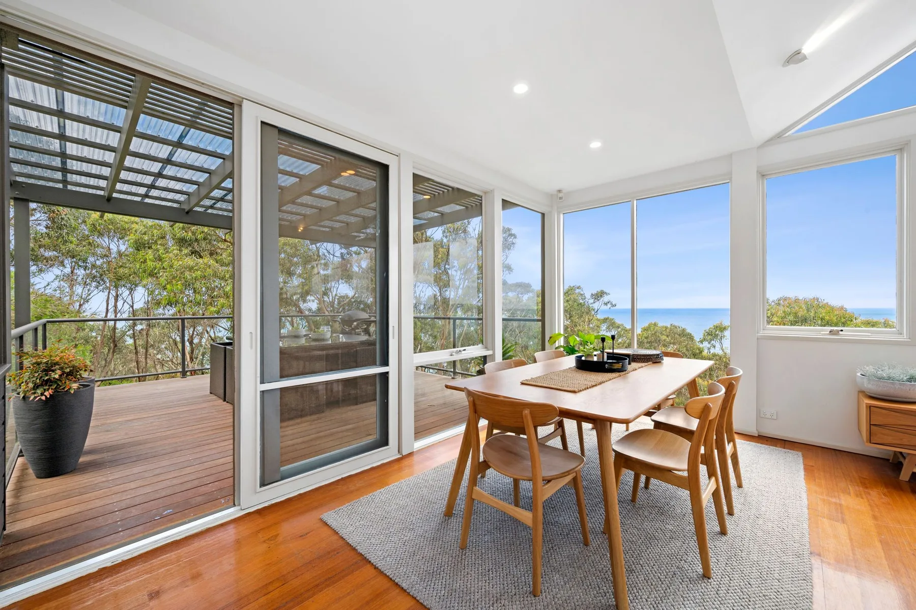 Un comedor luminoso con una mesa de madera junto a grandes ventanas con vistas a árboles y agua.