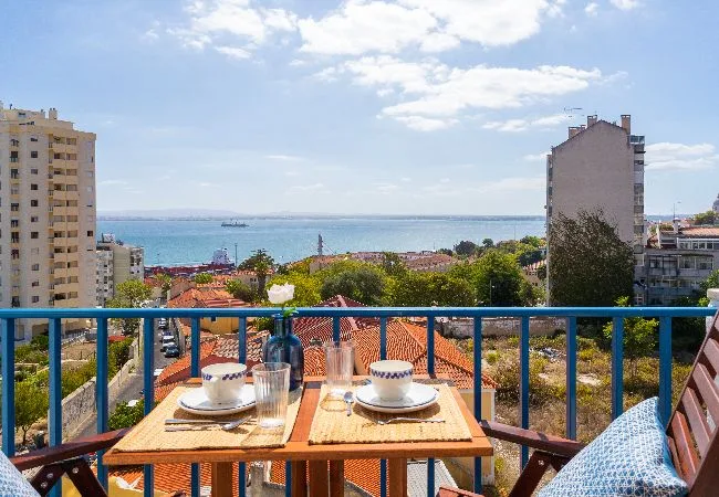 A balcony dining area overlooks red rooftops and the sea.
