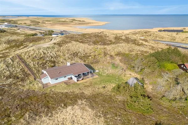 Una casa se encuentra entre dunas costeras con vistas a una amplia ensenada.