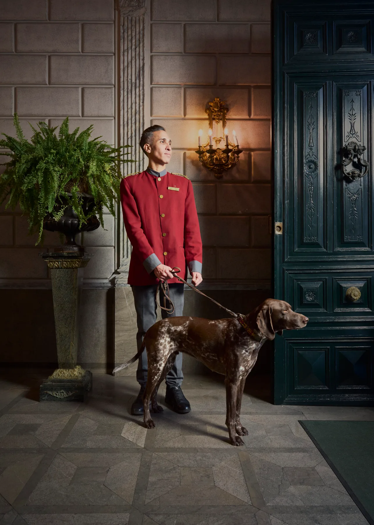Representative hotel space: A uniformed attendant stands with a dog beside a large entrance door.
