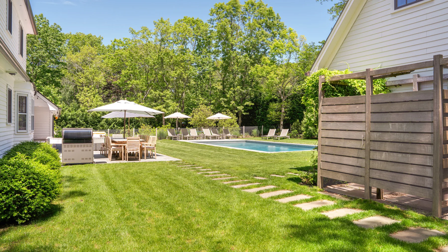 Un patio ajardinado con piscina, asientos y césped.