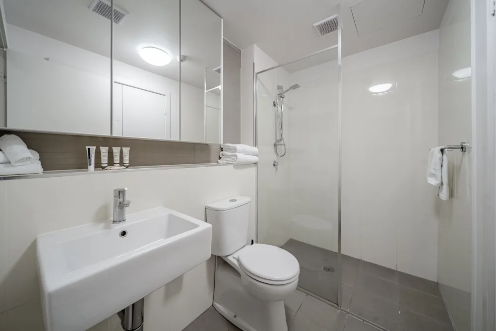 Un baño luminoso con lavabo suspendido, inodoro y ducha de vidrio.