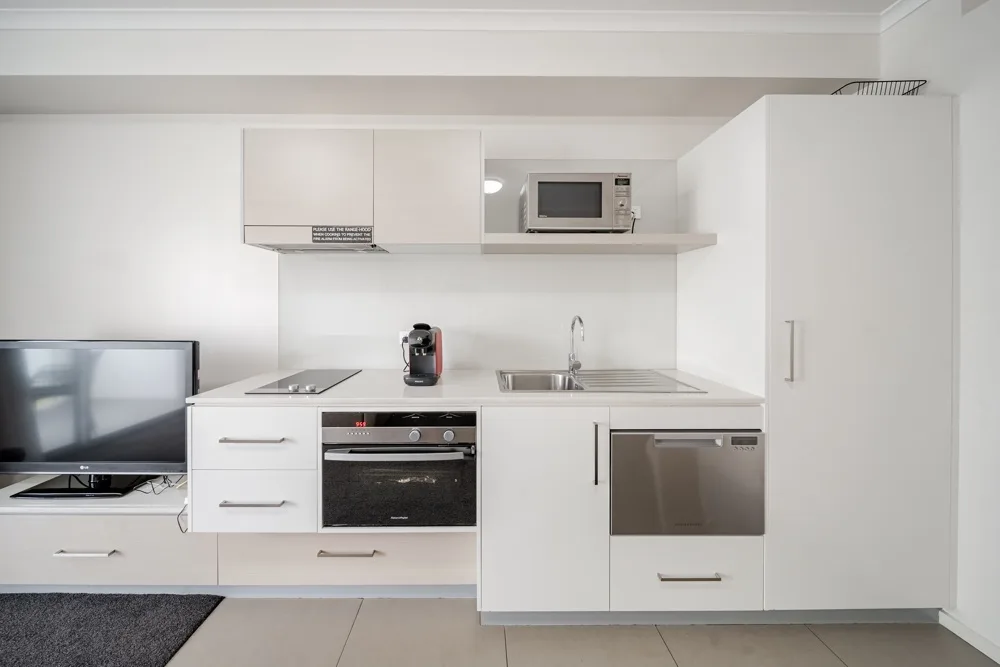 Una cocina blanca con encimera, electrodomésticos integrados y un televisor a un lado.