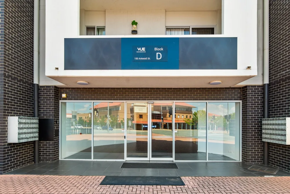 Zona común: Entrada del edificio con puertas de vidrio bajo un letrero azul.