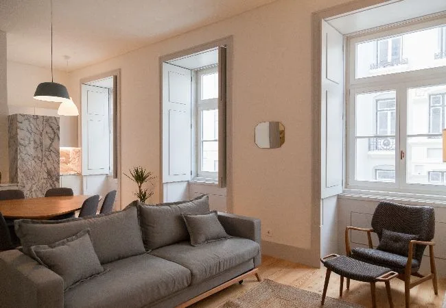 Una sala de estar con asientos grises, una mesa de comedor y ventanas grandes.