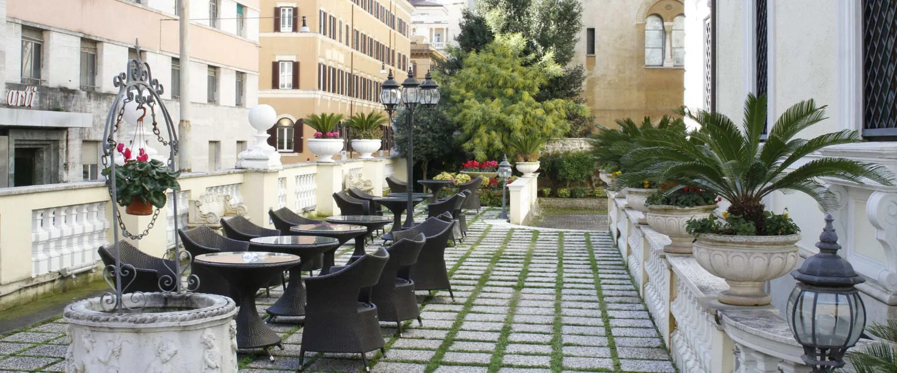 Representative hotel space: An outdoor terrace has café seating beside a paved walkway and potted plants.