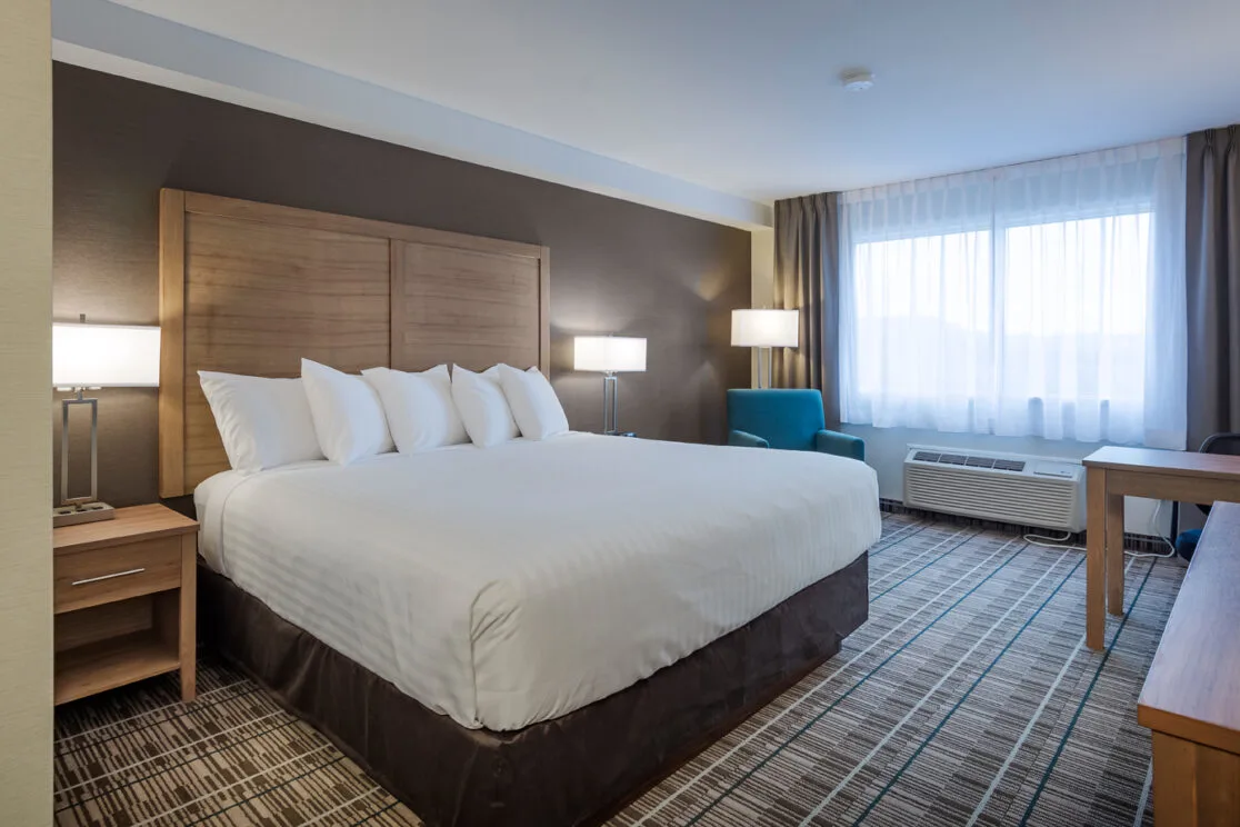 Espacio representativo del hotel: Dormitorio de hotel con una cama grande bajo un cabecero de madera.