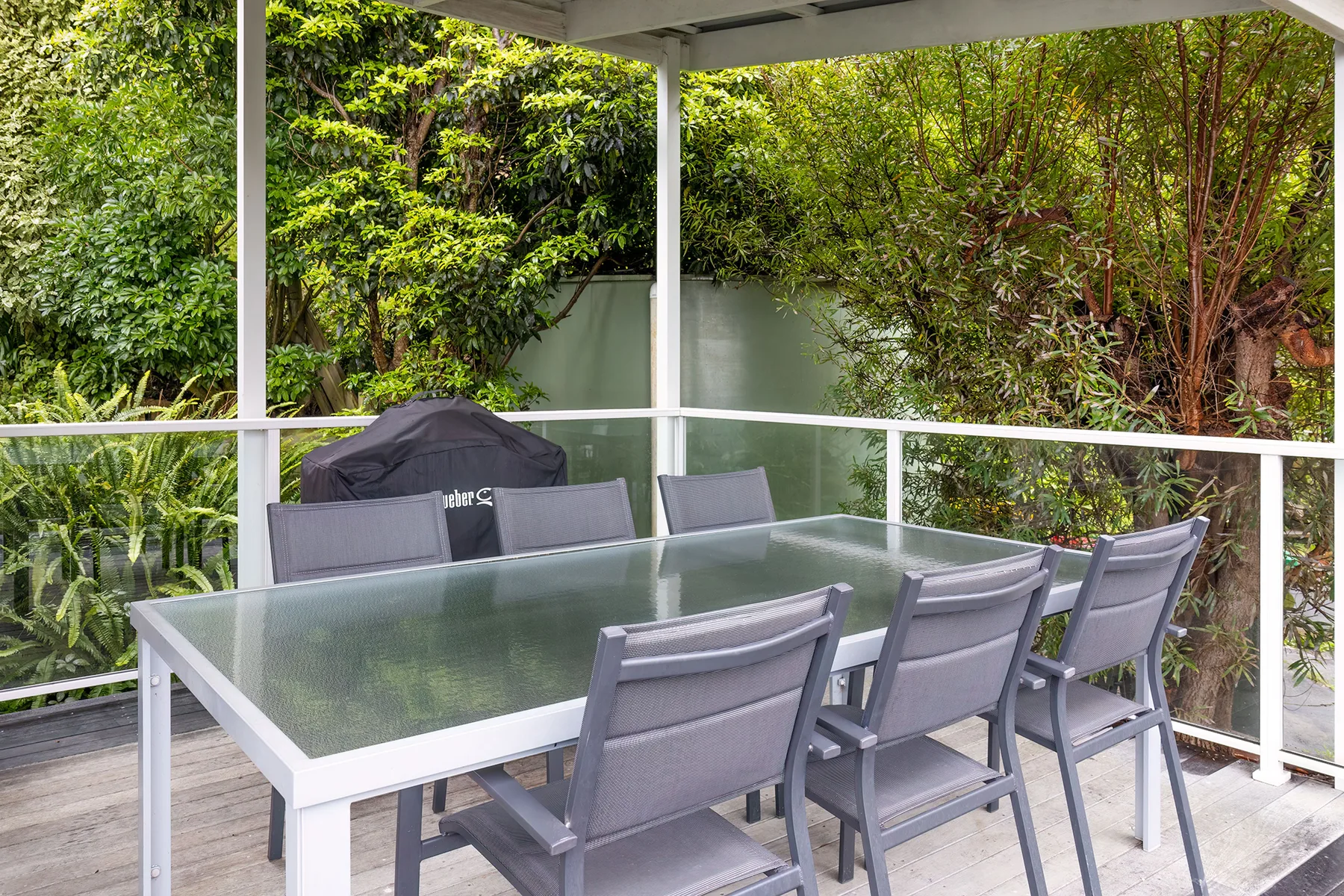 An outdoor dining area with a glass-top table and surrounding greenery.