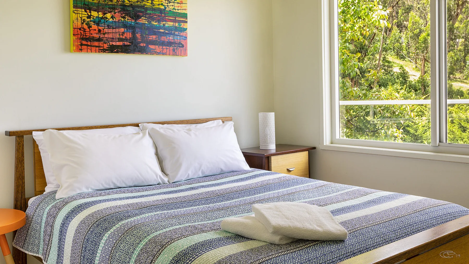 A bedroom with a neatly made bed and a large window overlooking greenery.