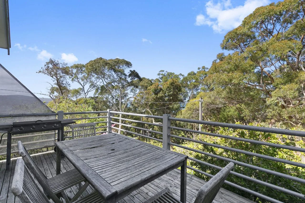An outdoor deck with a wooden table and seating overlooks leafy trees.